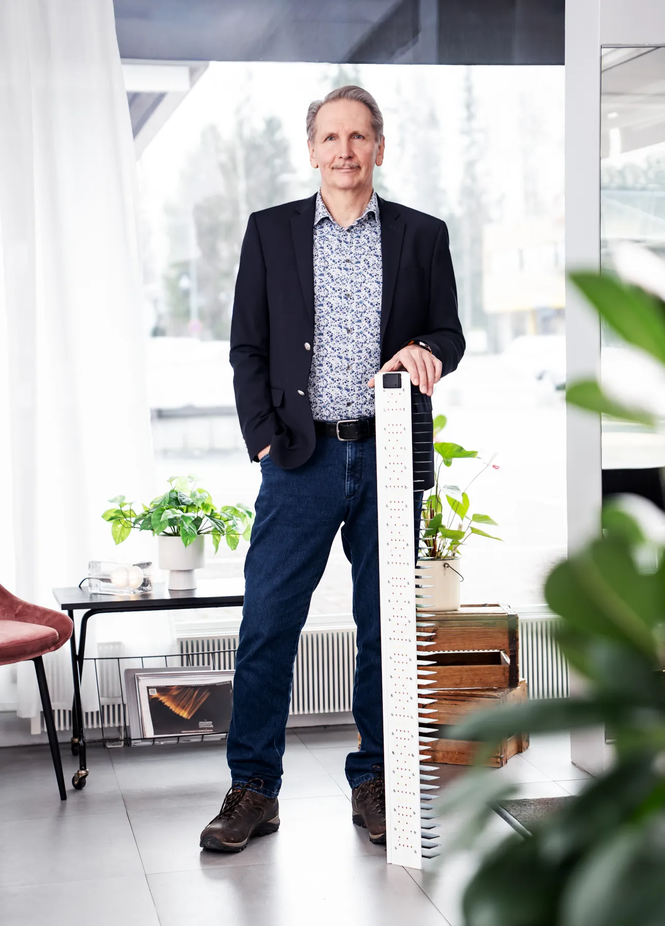 Mies seisoo sisätiloissa ja nojaa pitkään, valkoiseen valaisimeen, jossa on useita valopisteitä.